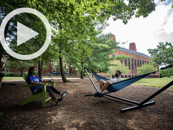 Two students lounging in a hammock and an adirondack chair.