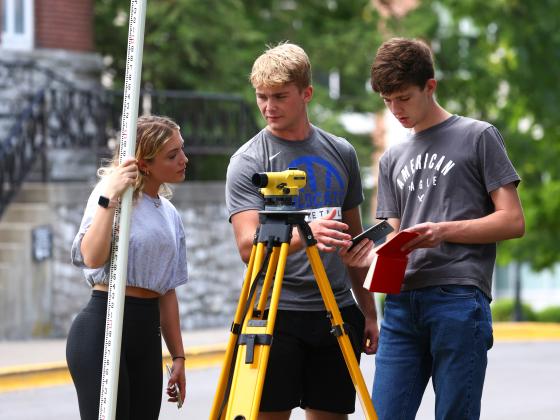 Three students with surveying machine practicing civil engineering