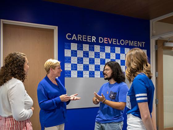 Staff member talking to 3 students in front of a sign that says "Career Development."