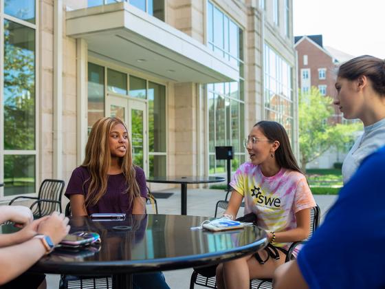 Students sitting outside at a table talking.